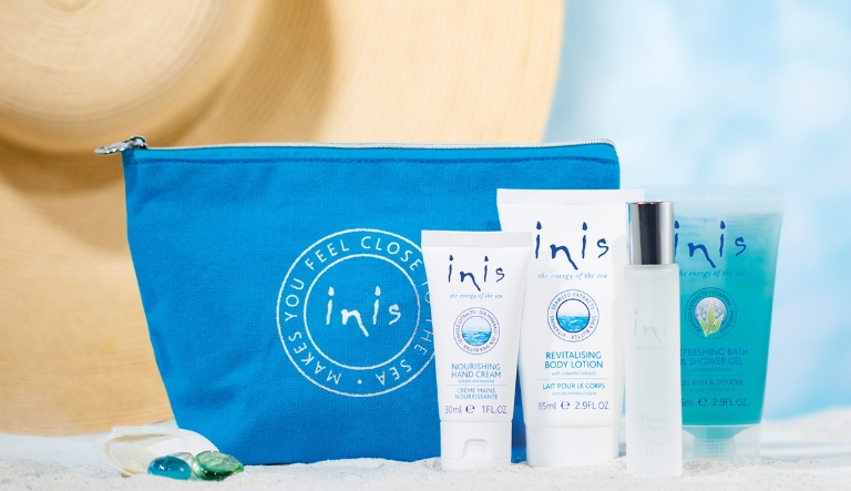 Front facing Lifestyle image of Inis Voyager Gift Set. Shows the four products included of body lotion, shower gel, hand cream and cologne with a blue fabric cosmetic bag, including the Inis logo on the front.